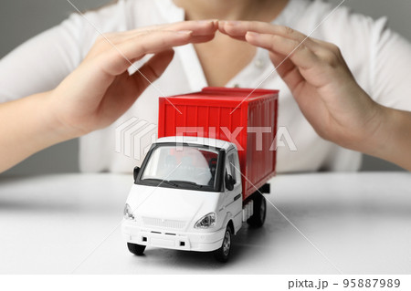 Woman covering toy truck at white table, closeup. Logistics and wholesale concept Woman covering toy truck at white table, closeup. Logistics and wholesale concept 95887989