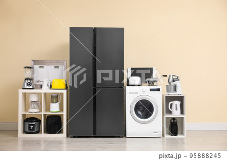 Modern refrigerator and other household appliances near beige wall indoors 95888245