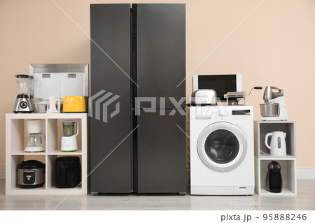 Modern refrigerator and other household appliances near beige wall indoors Modern refrigerator and other household appliances near beige wall indoors 95888246