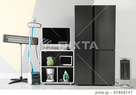 Modern refrigerator and other household appliances near color wall indoors 95888247