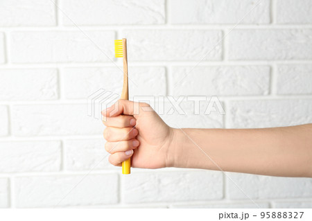 Woman holding bamboo toothbrush against white brick wall, closeup 95888327