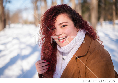 Portrait of a red-haired curly fat woman in the park in winter. Portrait of a red-haired curly fat woman in the park in winter. 95891235