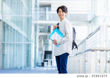 キャンパスの廊下でノートを持って立つ大学生の若い男性 95891974