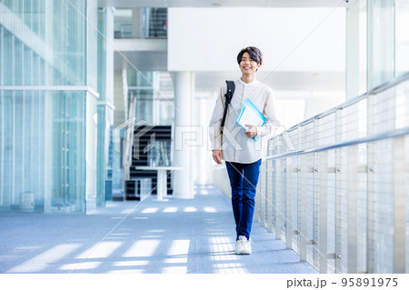 キャンパスの廊下でノートを持って立つ大学生の若い男性 95891975