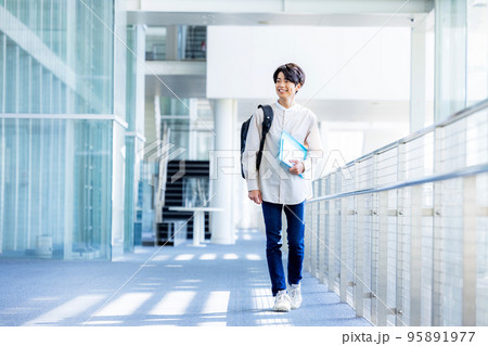 キャンパスの廊下でノートを持って立つ大学生の若い男性 95891977