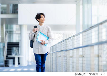 キャンパスの廊下でノートを持って立つ大学生の若い男性 キャンパスの廊下でノートを持って立つ大学生の若い男性 95891979