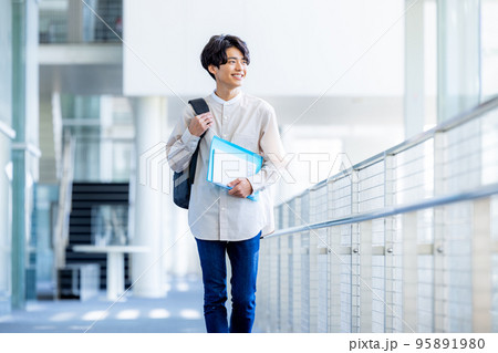 キャンパスの廊下でノートを持って立つ大学生の若い男性 キャンパスの廊下でノートを持って立つ大学生の若い男性 95891980