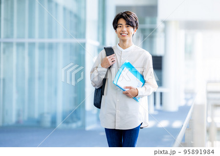 キャンパスの廊下でノートを持って立つ大学生の若い男性 95891984