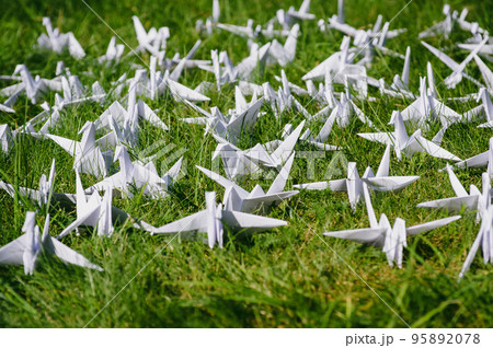 Japanese folded Origami cranes on fresh grass. Hundreds handmade paper birds on green field with copy space. 1000 thousand crane tsuru sculpture topic. Symbol of peace, faith, health, wishes and hope  95892078
