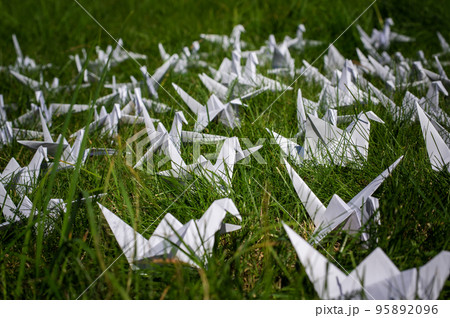 Japanese folded Origami cranes on fresh grass. Hundreds handmade paper birds on green field with copy space. 1000 thousand crane tsuru sculpture topic. Symbol of peace, faith, health, wishes and hope  95892096