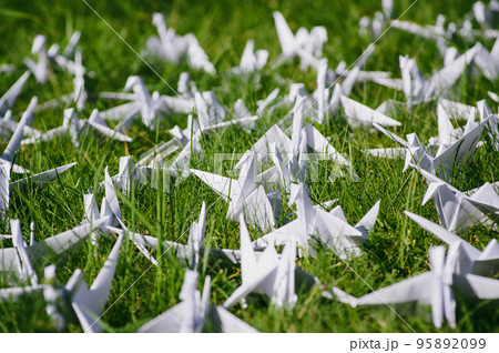 Japanese folded Origami cranes on fresh grass. Hundreds handmade paper birds on green field with copy space. 1000 thousand crane tsuru sculpture topic. Symbol of peace, faith, health, wishes and hope  95892099