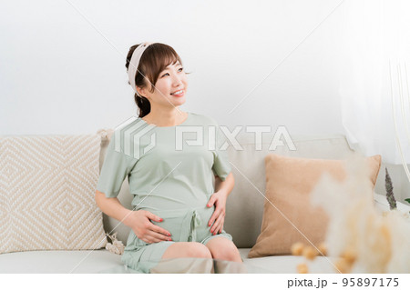 家でソファに座る笑顔の妊婦（アジア人女性） 95897175