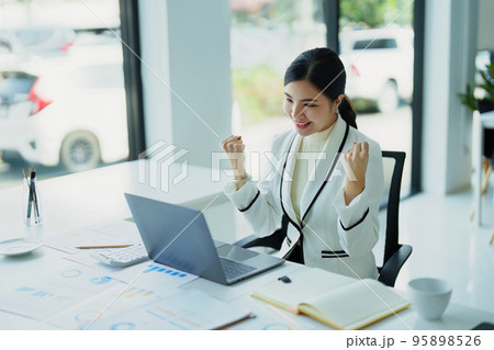 Portrait of a young Asian woman using a computer showing joy at the sales target. Portrait of a young Asian woman using a computer showing joy at the sales target. 95898526