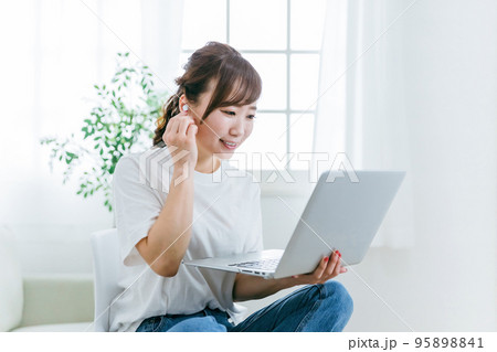 イヤホンを使いながらパソコンを使う笑顔の日本人女性（音楽・動画） 95898841