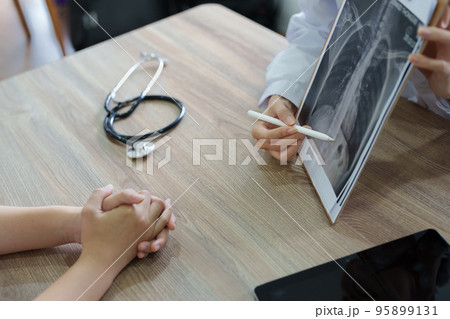 An Asian female doctor points to a patient x-ray film to explain the patient's treatment process. 95899131