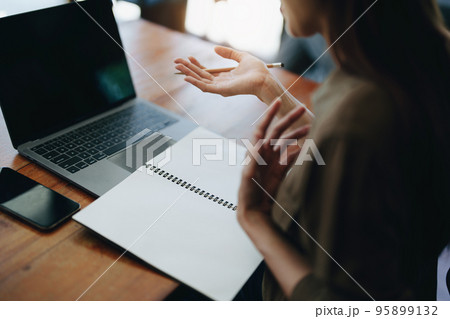 Portrait of a smiling Asian teenage girl wearing headphones and using a computer for online video conferencing in a library. 95899132