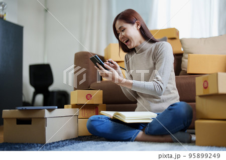 A portrait of a small startup, an SME owner, an Asian female entrepreneur checking orders to arrange the produce before packing the products in the inner boxes with the customers. Freelance concepts. 95899249