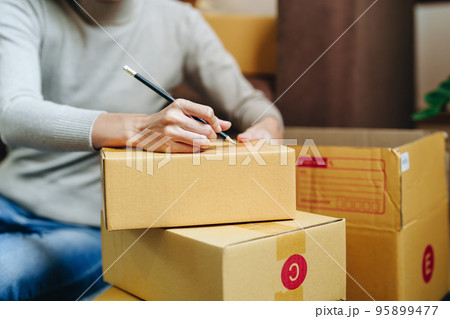 A portrait of a small startup, and SME owner, an Asian female entrepreneur, is writing down information on a box to organize the product before packing it into the inner boxes for the customer. 95899477