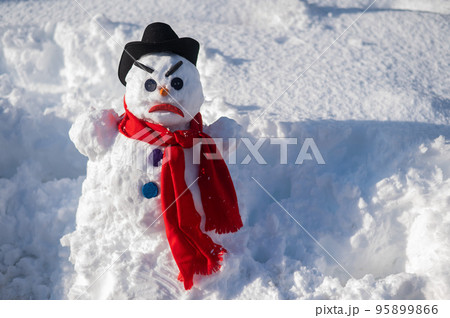A snowman with a creepy grimace in a hat and scarf. 95899866