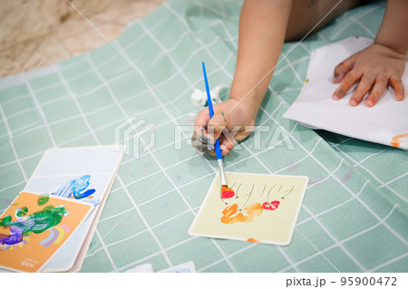 Focus on hands on paper. Children use paintbrushes to paint watercolors on paper to create their imagination and enhance their learning skills 95900472