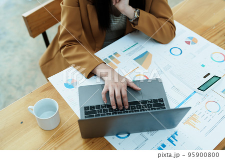 Portrait of a thoughtful Asian businesswoman looking at financial statements and making marketing plans using a computer on her desk. 95900800