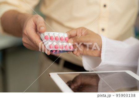 A young man receives pills from a pharmacist in a pharmacy. A young man receives pills from a pharmacist in a pharmacy. 95903138