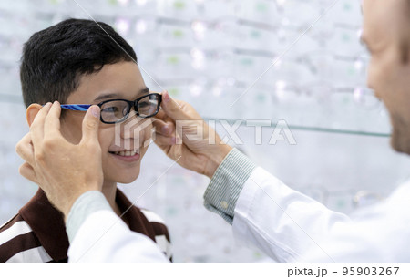 Ophthalmologist puts new eyeglasses on the boy. 95903267