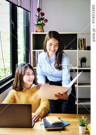 Two female company employees happily smiled at each other as they handed each other folders Two female company employees happily smiled at each other as they handed each other folders 95903980