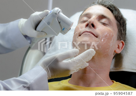 A white man gets a laser facial by a specialist. 95904587