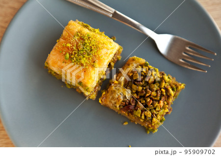 Baklava with pistachio, one of the most beautiful desserts of Turkish cuisine, in gray plate, on oak cutting board Baklava with pistachio, one of the most beautiful desserts of Turkish cuisine, in gray plate, on oak cutting board 95909702