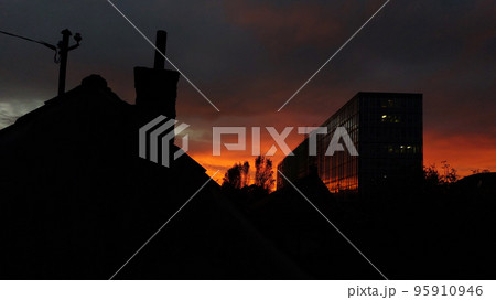 Red sky sunset in the urban environment, with silhouettes of one old house and one modern building, and trees between 95910946