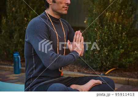 A man athlete, yogi in gray sportswear, sitting folded palms together, practicing yoga. Hands folded in prayer. Hands together. Prayer, gratitude. Yoga hand pose. Folded hands. Palm pressed. 95911413