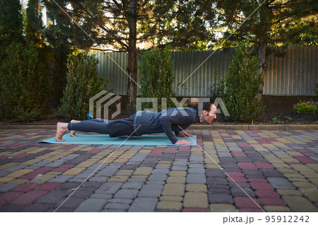 Side portrait of an active athlete Caucasian man yogi in his 40s, doing Yoga chaturanga push-ups on a fitness mat while practicing outdoors. Sport Fitness workout. Active and healthy lifestyle 95912242
