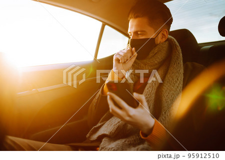 Young man in protective sterile mask in taxi car on a back seat checking her cell phone. Young man in protective sterile mask in taxi car on a back seat checking her cell phone. 95912510