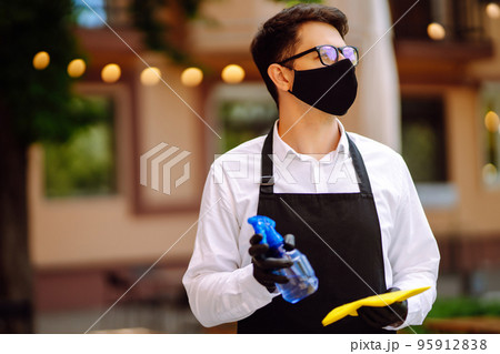 Disinfecting to prevent COVID-19. Waiter in protective face mask and gloves cleaning. Disinfecting to prevent COVID-19. Waiter in protective face mask and gloves cleaning. 95912838