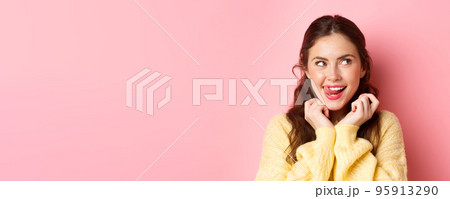Young devious girl licking her lips and teeth, looking aside with thoughtful face, having interesting idea, thinking, standing against pink background Young devious girl licking her lips and teeth, looking aside with thoughtful face, having interesting idea, thinking, standing against pink background 95913290