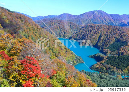 紅葉の山に囲まれたエメラルドグリーンの二居湖の秋風景 95917536