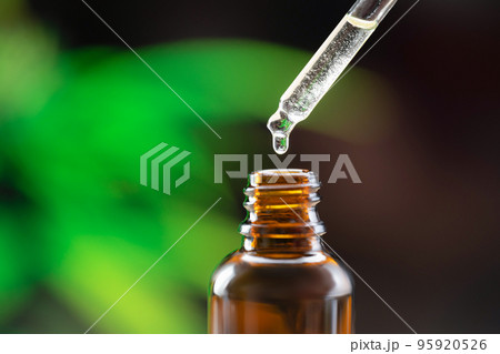 Closeup dropper with legalized CBD oil at the tip, near to the CBD oil container 95920526