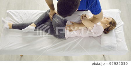 Male physiotherapist provides physical assistance to female patient with back and leg injuries. 95922030