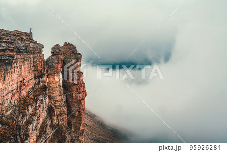 Awesome caucasus landscape with silhouette of hiker above white clouds and Rocks of Big Bermamyt - the so-called "Monks".  Man with backpack in high mountains. Panoramic view. 95926284