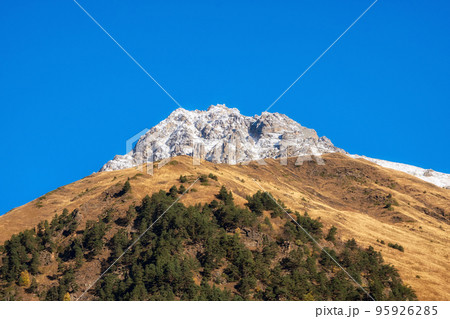 Autumn snow mountains at noon. Bright mountain landscape with a snowy rock in golden sunlight. Natural background of a walk through the rocky mountains with sharp rocks and blue sky. 95926285