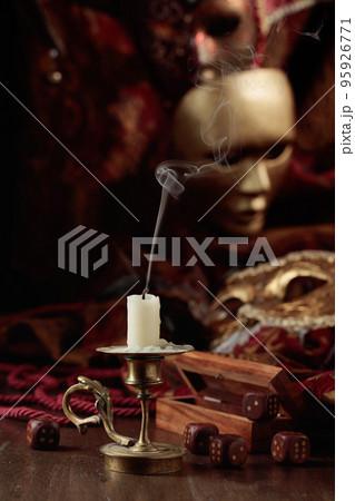 Extinguished candle, dice, and carnival masks on an old wooden table. 95926771
