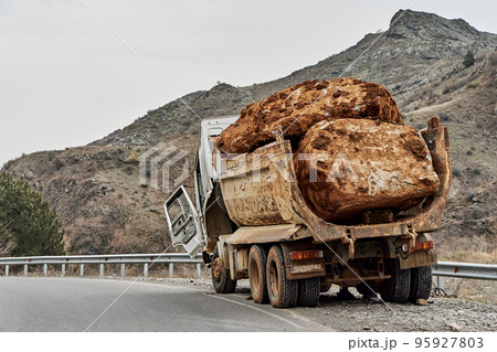 An old truck carrying a huge stone in the back broke down on a mountain road 95927803