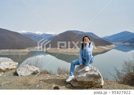 A girl poses against the background of the Zhinvali reservoir while traveling in Georgia. Incredible natural landscape A girl poses against the background of the Zhinvali reservoir while traveling in Georgia. Incredible natural landscape 95927922