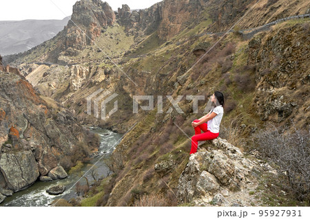 A girl poses on a cliff with a breathtaking view of the gorge in which the river flows. Picturesque photos of mountains A girl poses on a cliff with a breathtaking view of the gorge in which the river flows. Picturesque photos of mountains 95927931