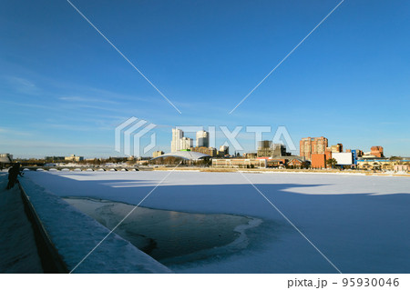 Panorama of a frozen river and buildings illuminated by the sun on a winter day against a blue sky Panorama of a frozen river and buildings illuminated by the sun on a winter day against a blue sky 95930046