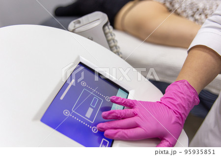 A medic adjusts the operating mode of the anti-cellulite massage machine with compression and vibration technology in beautician office. 95935851