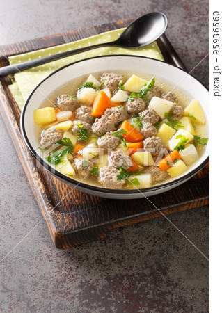 Sodd is a traditional Norwegian soup made with cooked mutton and meatballs and potatoes, carrots are included in a clear, fragrant broth closeup in the plate. Vertical Sodd is a traditional Norwegian soup made with cooked mutton and meatballs and potatoes, carrots are included in a clear, fragrant broth closeup in the plate. Vertical 95936560