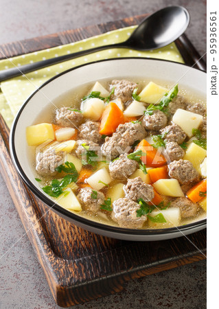 Traditional Norwegian soup Sodd with root vegetables and beef meatballs close-up in a plate. Vertical 95936561