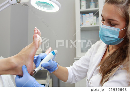 A pedicure master treats the heel with a power tool in a beauty salon. A pedicure master treats the heel with a power tool in a beauty salon. 95936648